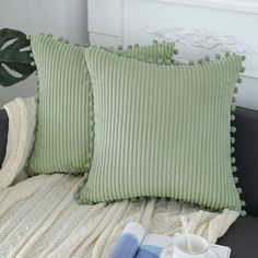 two green pillows sitting on top of a couch next to a cup and saucer