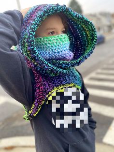 a young boy wearing a colorful crocheted scarf with a face mask covering his mouth