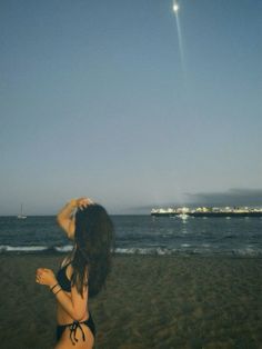 a woman standing on top of a beach next to the ocean under a blue sky