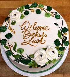 a white cake with green leaves and flowers on it that says welcome baby lind