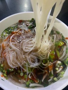 a bowl filled with noodles, vegetables and sauce being drizzled over it