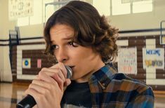 a young man holding a microphone up to his mouth while standing in front of a basketball court