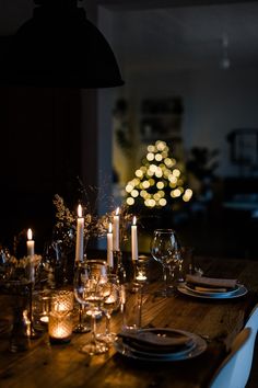 a wooden table topped with plates and glasses next to a lit christmas tree in the background