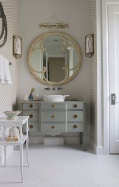 an image of a bathroom setting with white furniture and gold accents on the mirror above the sink