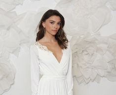 a woman wearing a white dress standing in front of a wall with flowers on it