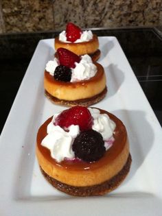 three desserts are arranged on a long white platter with berries and whipped cream