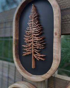 a wooden plaque with a pine tree cut out on it's side, hanging from a fence