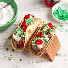 two tacos with toppings sit on a cutting board next to some condiments