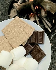 marshmallows and graham crackers on a plate next to a campfire