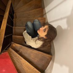 a young woman sitting on the bottom of a wooden staircase looking up at the camera