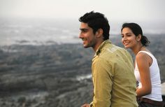 a man and woman standing next to each other on top of a hill looking at the camera