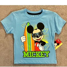 This Fun Disney Mickey Mouse T-Shirt Is Perfect For Little Beach Lovers! Available In Many Sizes, It Features A Cute Surfing Beach Theme That Any Toddler Boy Will Love. Made With Quality Materials And Featuring The Beloved Disney Character, This T-Shirt Is Sure To Become A Favorite. Disney Crew Neck T-shirt For Summer, Playful Cartoon Print T-shirt For Disney Trips, Disney Summer Cartoon Print T-shirt, Disney Character Print Summer T-shirt, Mickey Mouse Tops For Disney Trips In Summer, Themed Cartoon Print Tops For Disney Trips, Playful Cotton Mickey Mouse T-shirt, Themed Mickey Mouse Short Sleeve T-shirt, Mickey Mouse Themed Short Sleeve T-shirt