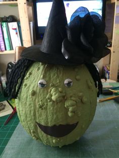 a green pumpkin with a black hat on it's head, sitting on a table