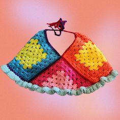 a multicolored crocheted item hanging from a hook on a pink background