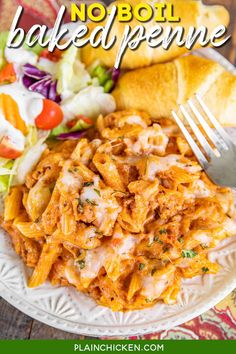 a white plate topped with pasta and meat covered in sauce next to a roll on a wooden table