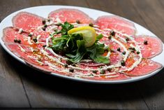 a white plate topped with slices of meat covered in sauce and garnishes