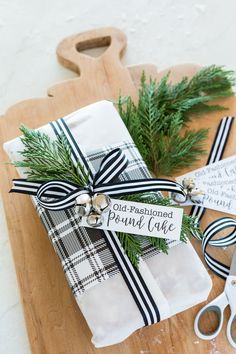 a wooden cutting board topped with two wrapped present boxes next to scissors and pine needles