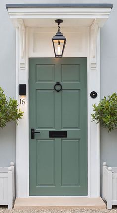 a green front door with two planters on either side and a light above it