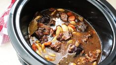 a crock pot filled with beef stew and carrots on top of a table