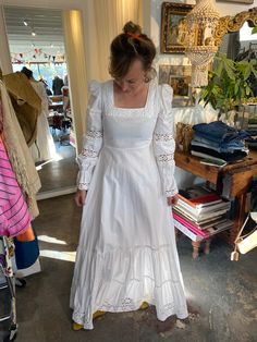 a woman in a white dress is looking down at her hand on the ground while standing next to a pile of books