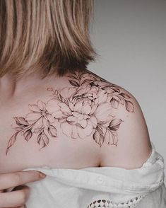 the back of a woman's shoulder with flowers and leaves tattooed on her chest