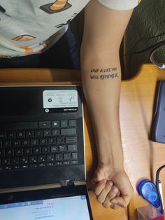 a person with a tattoo on their arm next to a laptop