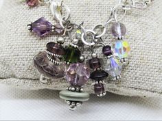 "This ARTISAN GLASS (Lampwork) BRACELET features 3 BOROSILICATE GLASS BEADS in shades of purple and green. The Boro glass beads are roughly 8x15mm and are spaced throughout the bracelet. There are also 10x14mm crystal tapered faceted ovals in purple and 8x12mm faceted crystal rondelles in the same purple; 5x8mm silver spacer beads, along with assorted clear and lavender faceted crystals. There are 7 assorted drops on the chain, inclding lampwork rondelles, Swarovski crystals, other glass, crysta Handmade Purple Glass Bracelets, Hand-strung Adjustable Czech Glass Stretch Bracelet, Hand-strung Czech Glass Crystal Bracelet As Gift, Useable Gifts, Artisan Hand-strung Czech Glass Beaded Bracelets, Adjustable Czech Glass Crystal Bracelet, Hand-strung, Lampwork Bracelets, Farmers Market Bag, Green Bracelet