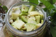 a glass jar filled with sliced apples on top of a wooden table next to leaves