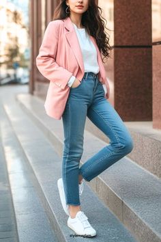 a woman standing on some steps wearing jeans and a pink blazer with white sneakers