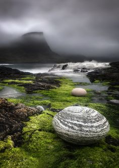 two rocks sitting on top of green moss covered ground next to water and mountains in the background