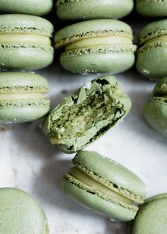 green macaroons with one bite taken out and the other half open on a white surface