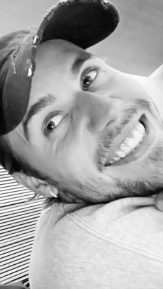 a black and white photo of a man with a baseball cap on smiling at the camera