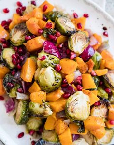 a white plate topped with brussel sprouts, squash and pomegranate