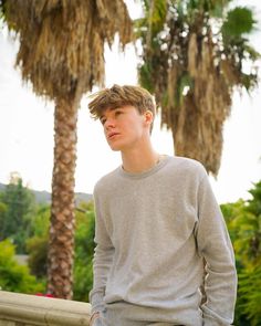 a young man is standing in front of palm trees and looking off into the distance