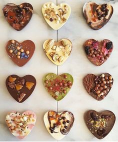 twelve heart shaped chocolates are arranged on a white marble counter top, each with different toppings