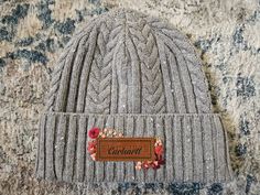 a gray cable knit beanie with a leather tag on it sitting on a rug