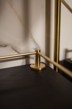 a close up of a black table with a gold metal frame and marble wall in the background