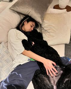 a woman laying on top of a couch next to a black dog in her lap