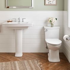 a white toilet sitting next to a sink in a bathroom under a mirror and towel rack