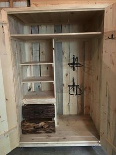 an unfinished wooden cabinet with shelves and hooks on the door, in a room that is being built