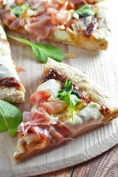 two slices of pizza sitting on top of a wooden cutting board next to green leaves