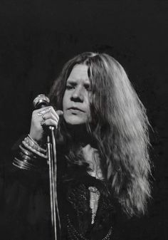 a woman with long hair holding a microphone in her hand and looking off to the side