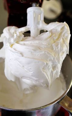 a metal bowl filled with white frosting next to a blender on top of a counter