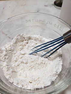 a glass bowl filled with flour and whisks