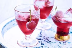 two glasses filled with ice and cherries sitting on a blue and white tablecloth