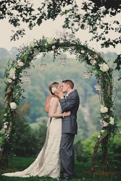 a couple kissing in front of an arch with flowers and greenery on the side