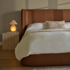 a bed with white sheets and pillows on top of it next to a night stand