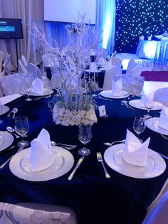 the table is set with white plates and napkins, silver place settings and centerpieces