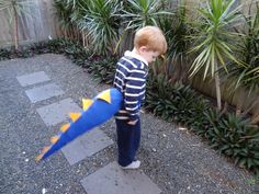 a young boy standing next to a blue and yellow dragon kite in front of some plants