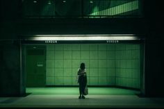 a woman standing in an empty room with green lights on the ceiling and doors open